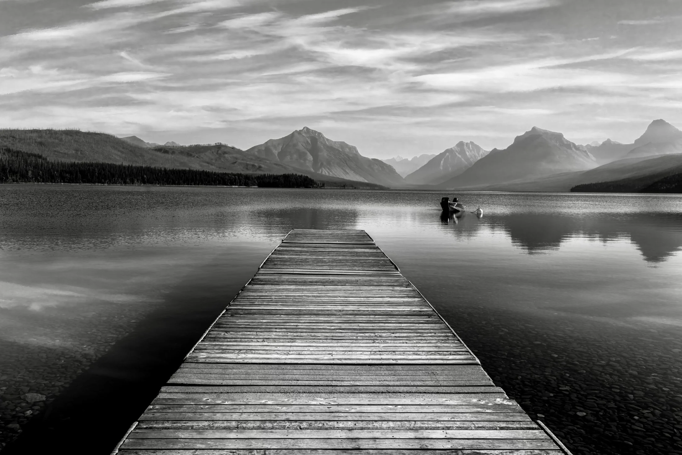 A wooden dock looking toward a still lake and Montana mountain peaks