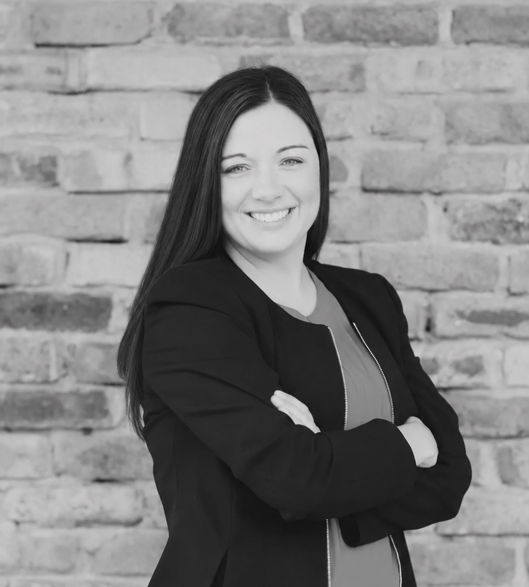 Kelly Cuffe standing with arms crossed in front of a brick wall
